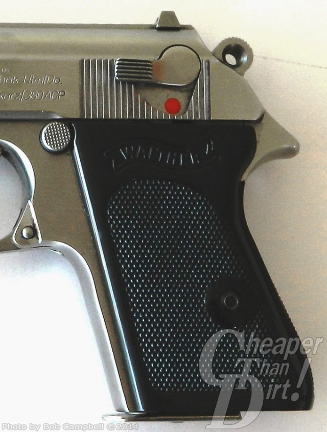 Black-handled, silver barreled Walther PPK, barrel pointed to the left, with focus on the slide mounted safety on a white background