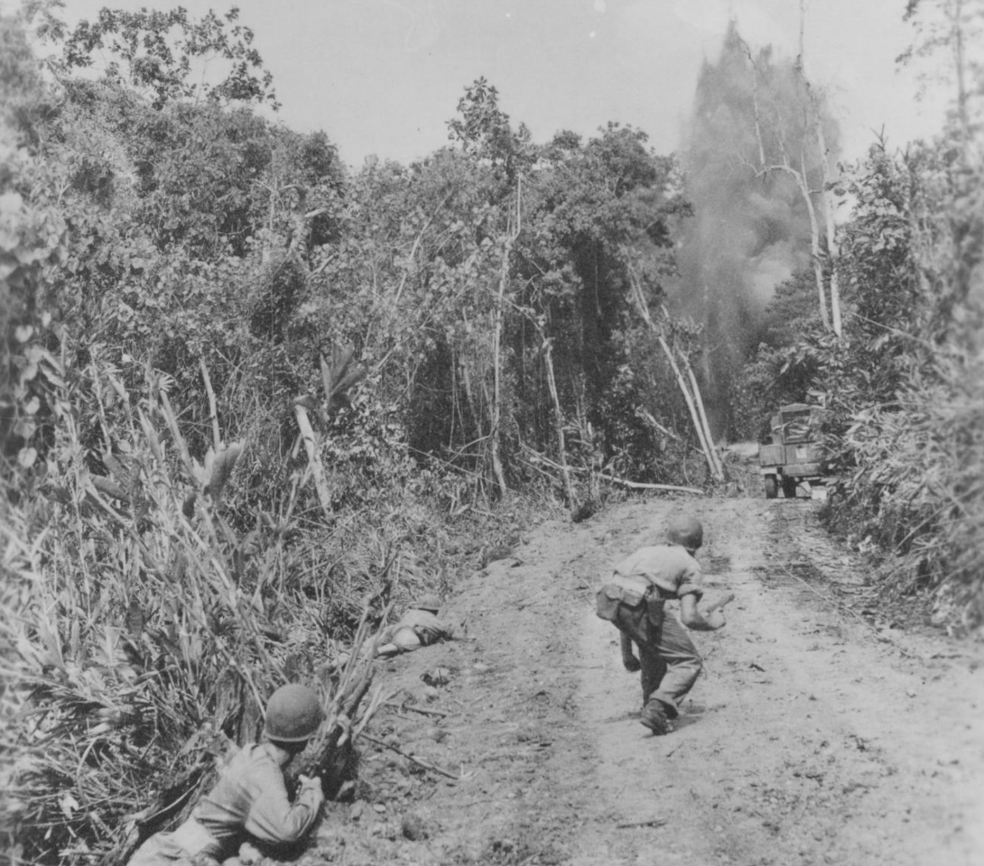 US soldiers advance along a road on Guadalcanal while an explosion is visible in front of them