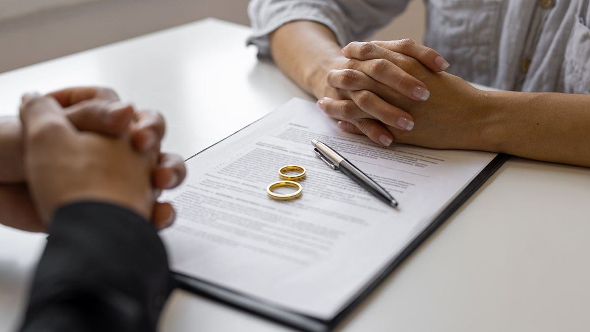 Couple sitting across from each other with divorce papers and wedding rings