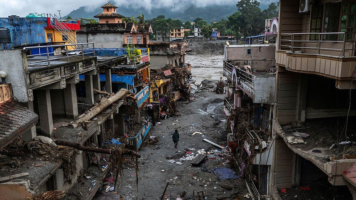 A man walks next to mud-covered damaged buildings near the Likhu River in Nepal.