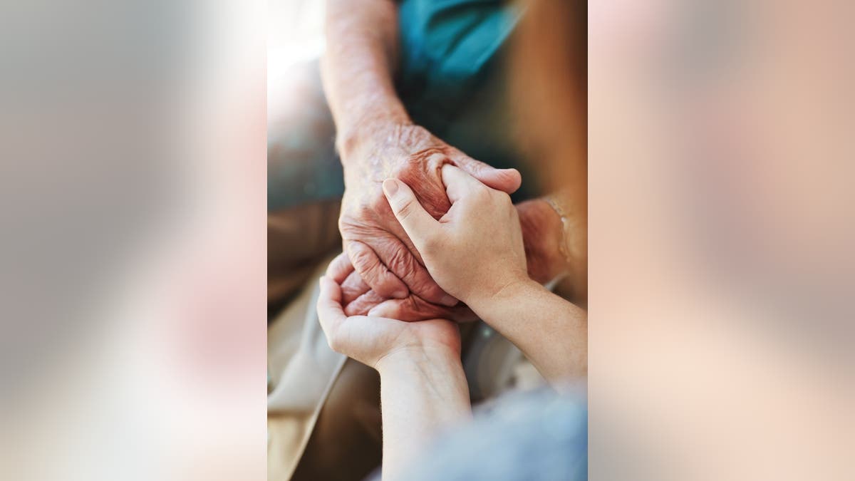 Woman holds a senior man's hands in comfort.