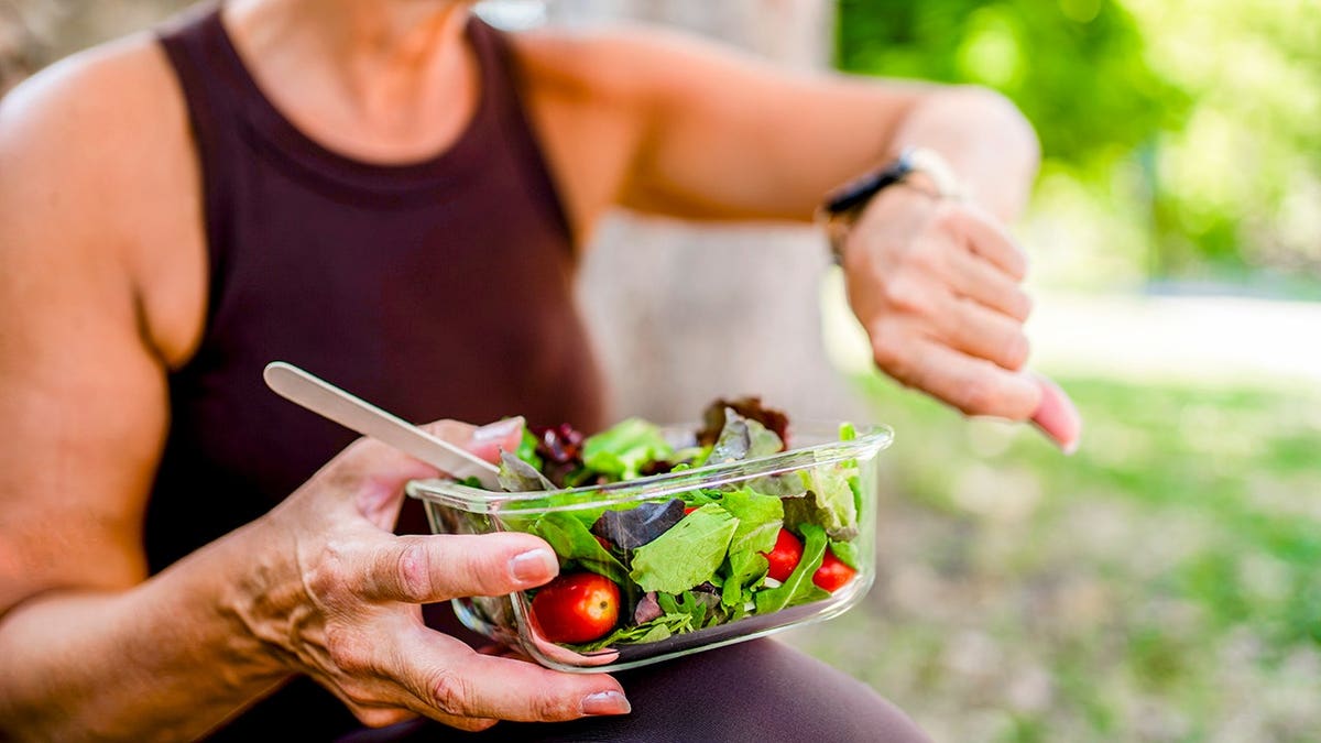 Woman holding a fresh salad while checking her smartwatch outdoors.