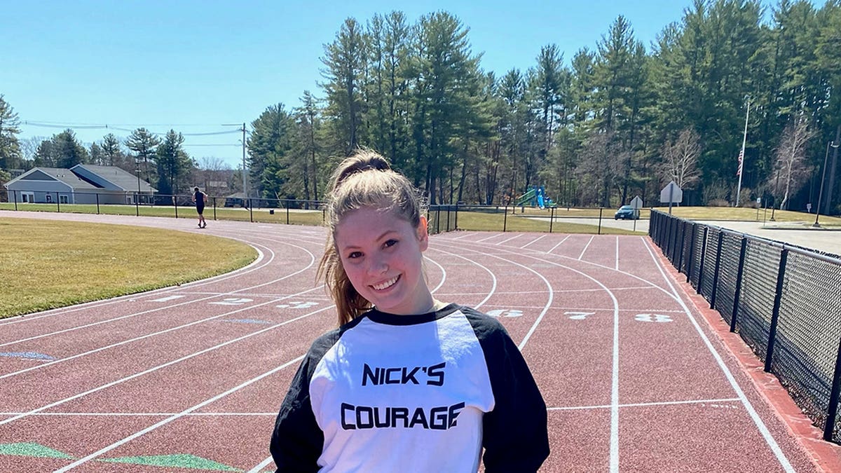 Ashlyn Mercier on a track field holding a Nick's Courage sign.