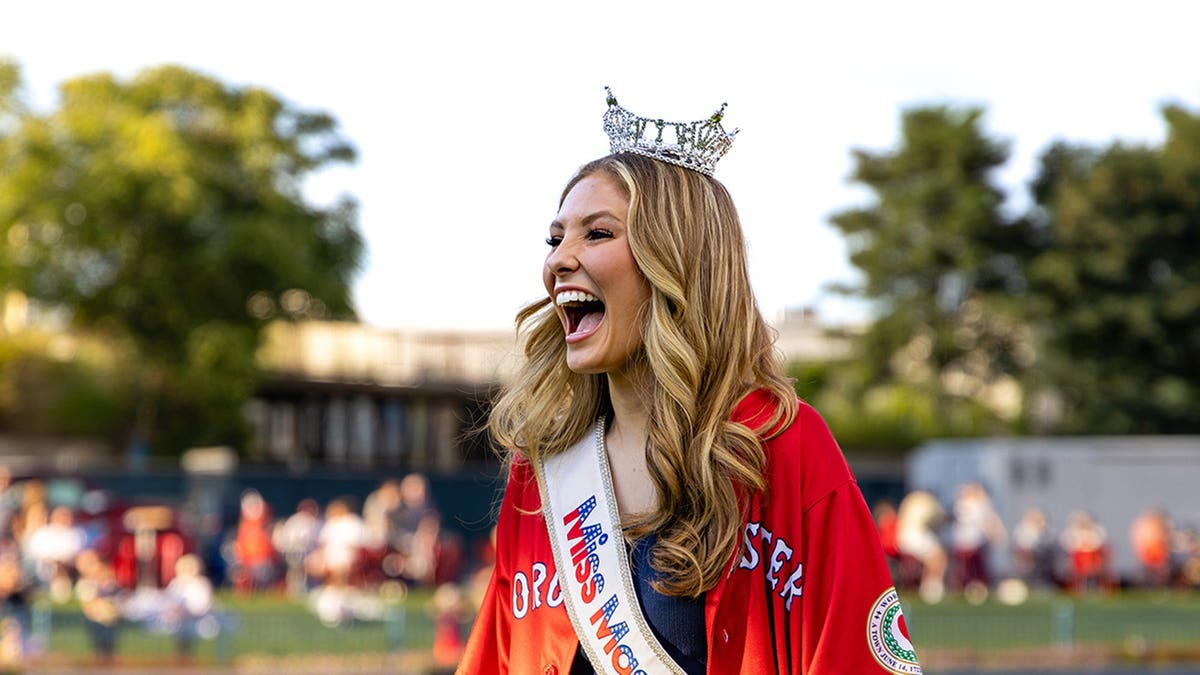 Ashlyn Mercier in a red dress, sash and gown cheering to a crowd.