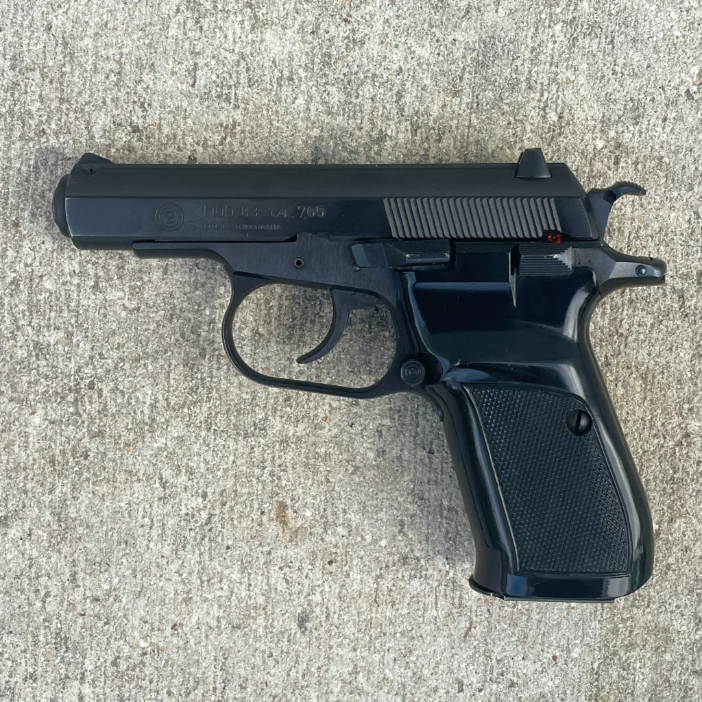 A black semi-automatic pistol with a textured grip and iron sights, resting on a concrete surface.