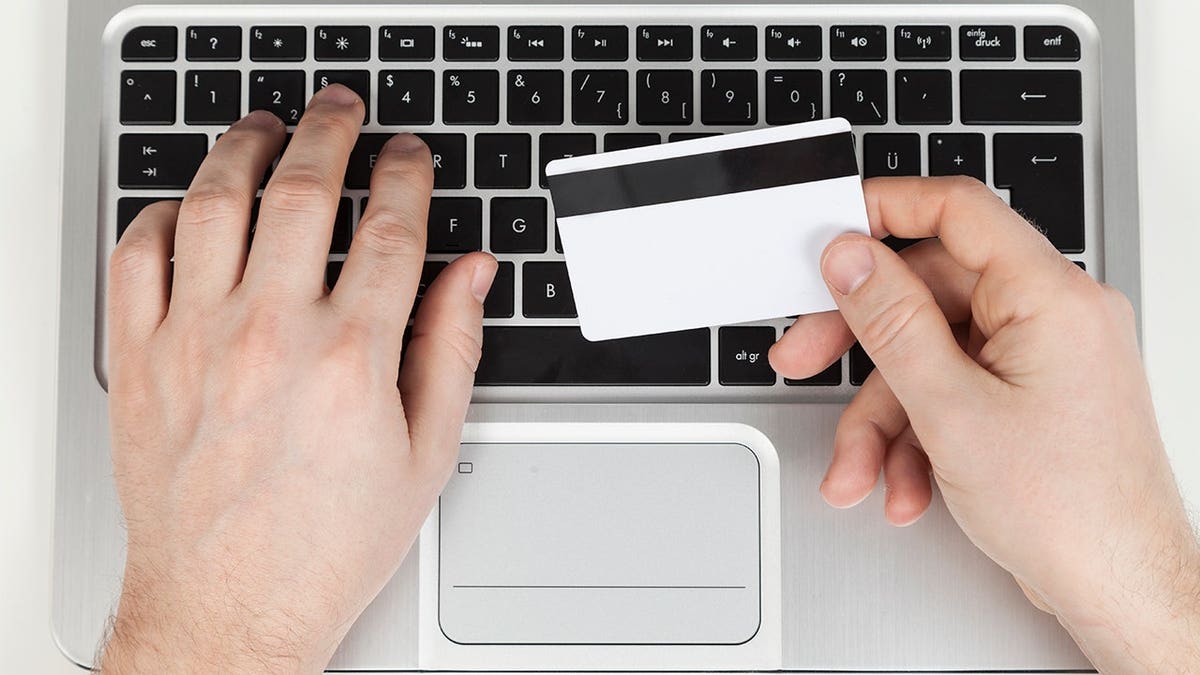 Person holding their credit card while typing on their computer.