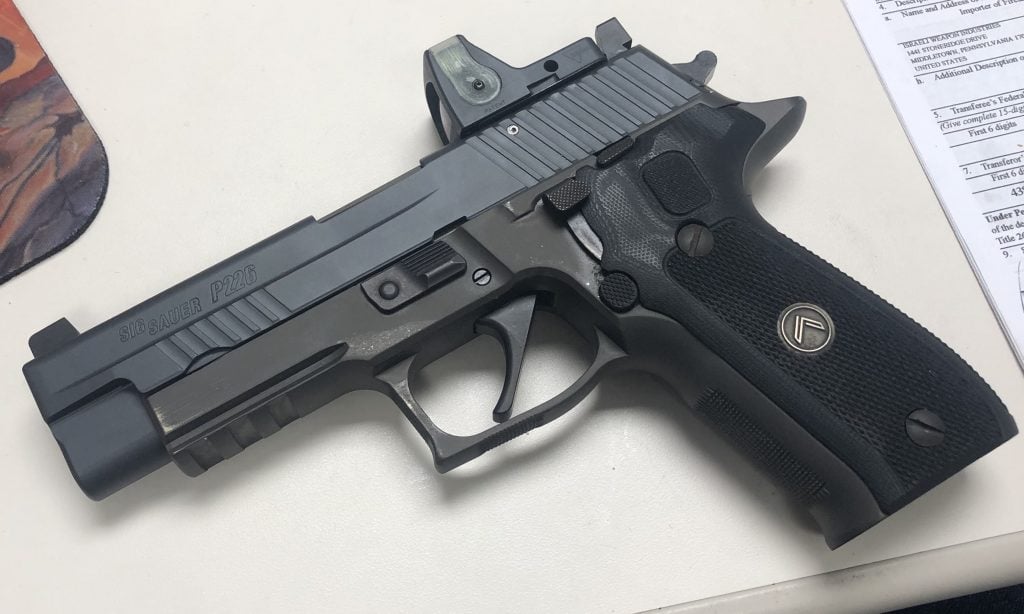 "Sig Sauer P226" pistol with an optic mounted on the slide, resting on a desk.