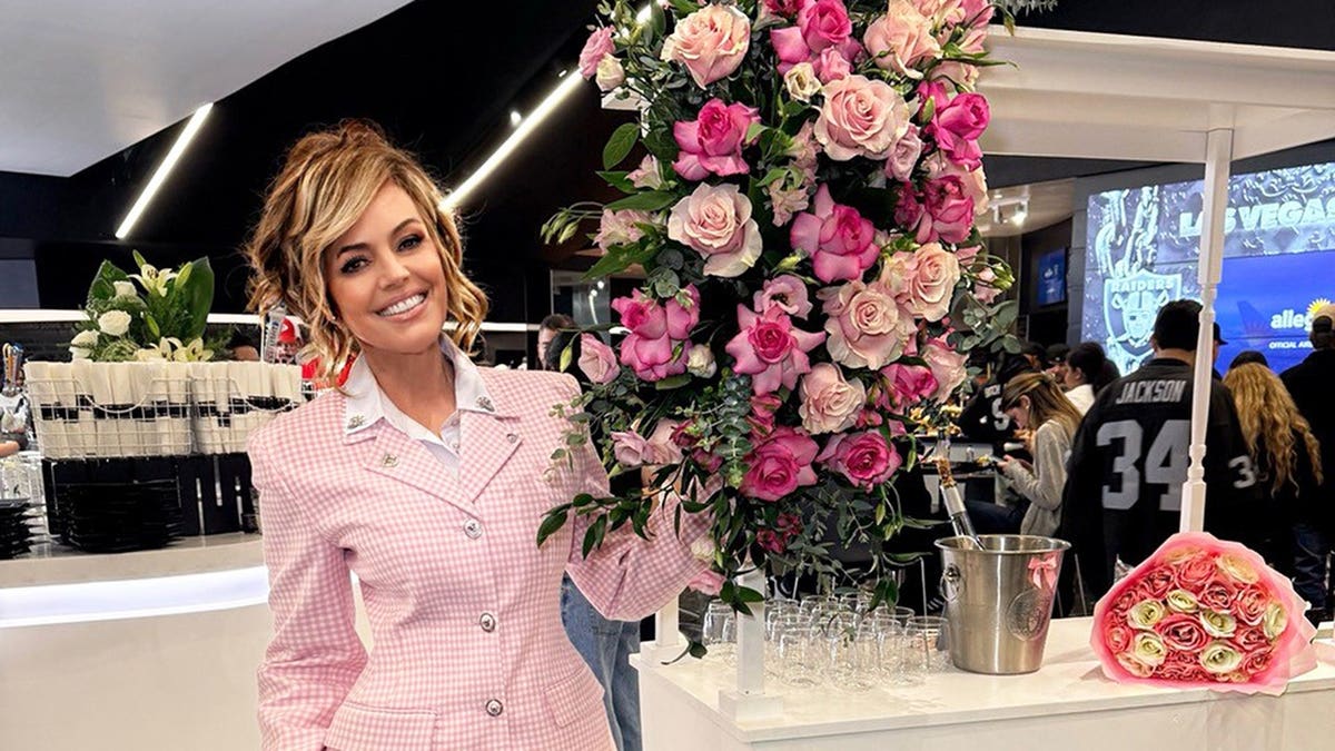 Sandra Taylor in a pink suit near a booth with flowers.