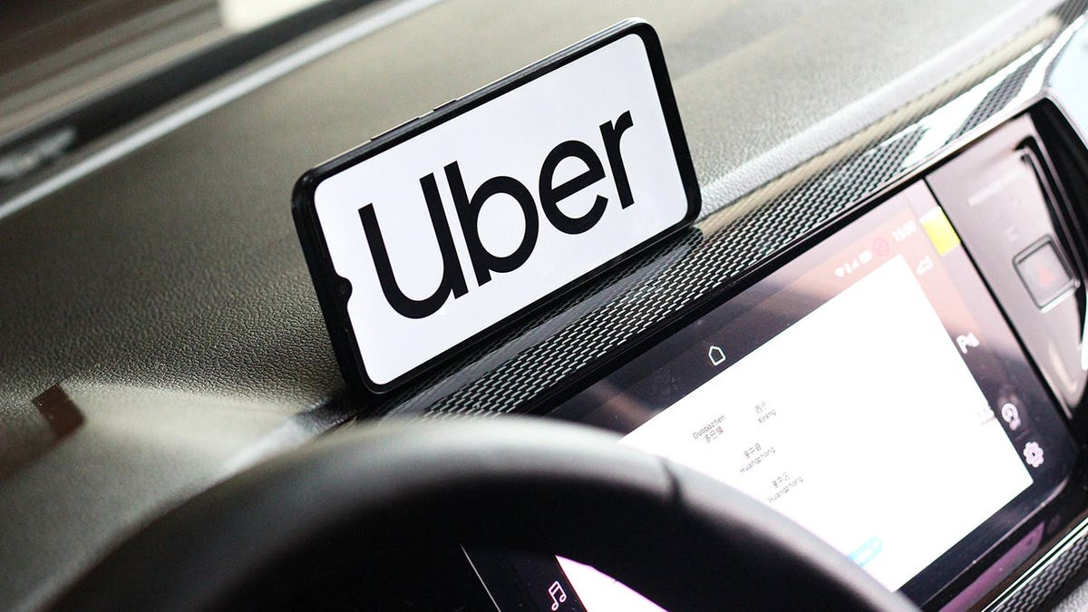 A phone on the dashboard of a vehicle with the Uber logo pulled up.