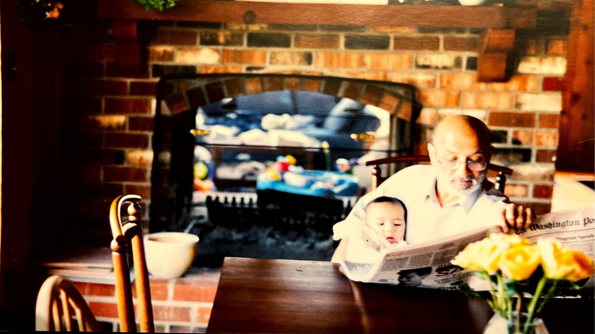 Zafar Nomani holds his grandson in his arms as he reads the newspaper.