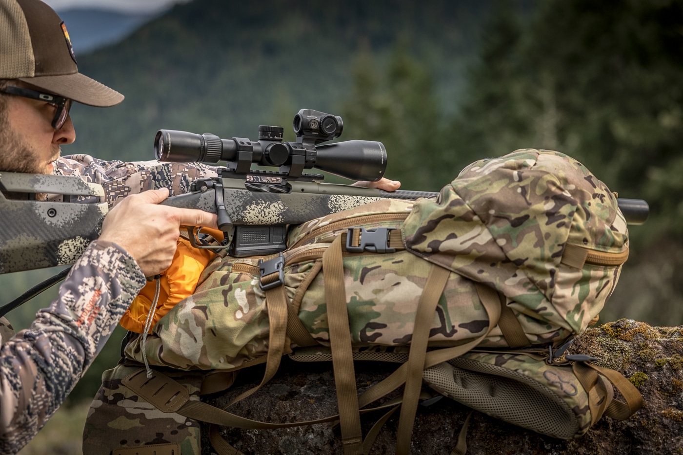 author using his scope mounted red dot sight in the field from an improvised rest using his backpack
