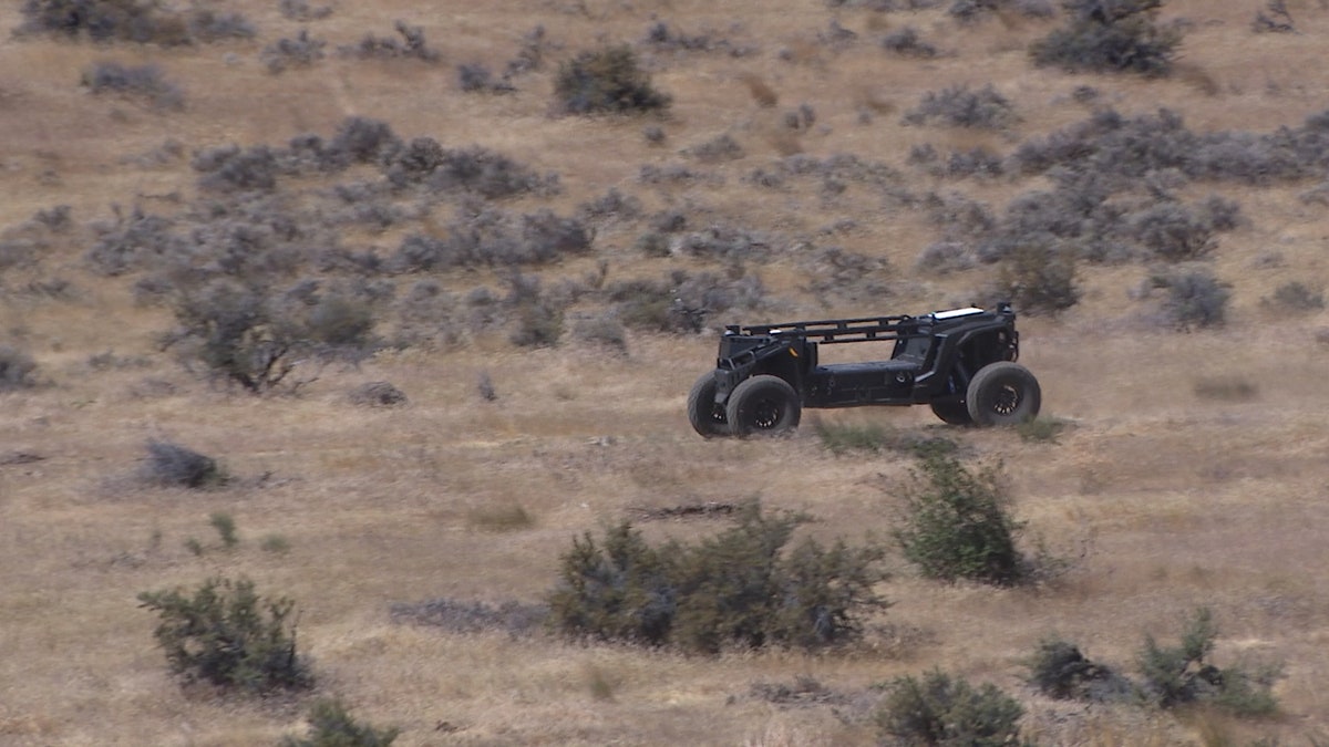 A driverless Overland AI ground vehicle moves through a dry, brush-covered landscape during an off-road demonstration.