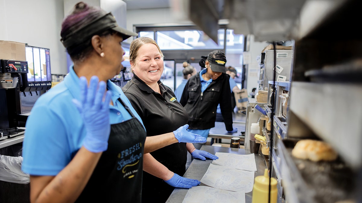 An employee at Biscuitville smiles while talking to another employee.