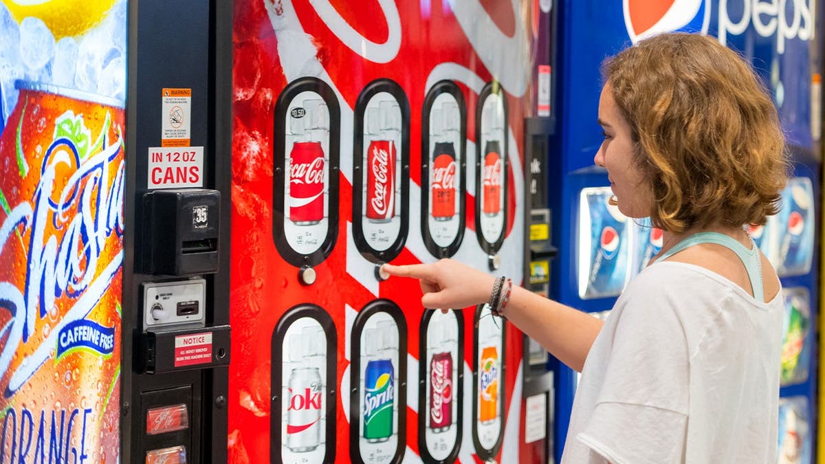 A woman selects a soda from a vending machine.