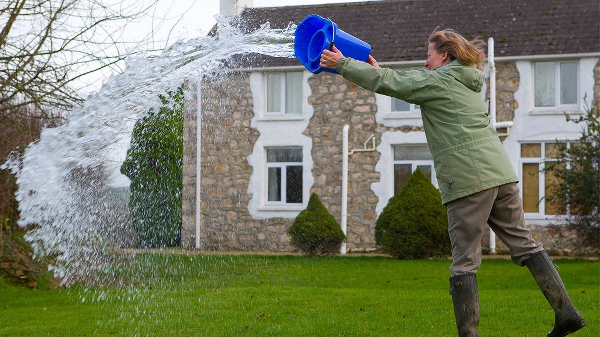 A woman throws out a bucket of standing water.