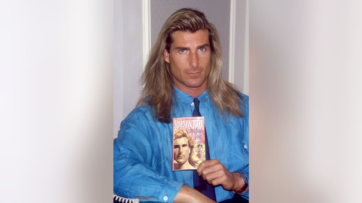Fabio Lanzoni holds Brenda Joyce's book Scandalous Love in a portrait.