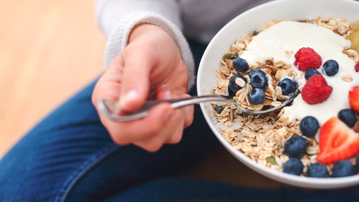 A person eats a bowl of oats with fruit.