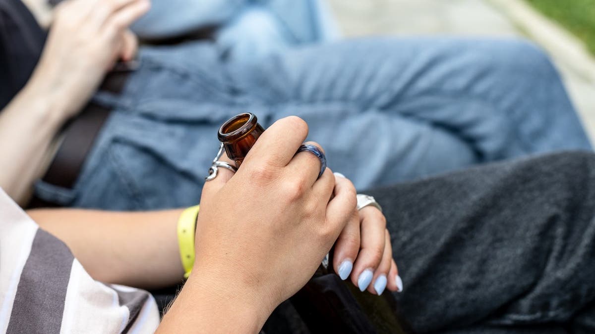 Girl's hands hold the neck of an open glass bottle outdoors.