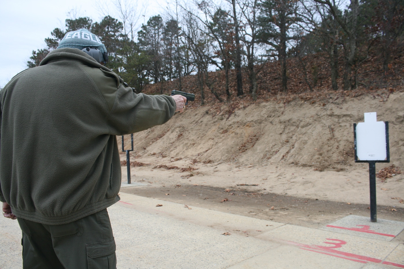 man on range shooting a pistol at a target with a one handed hold
