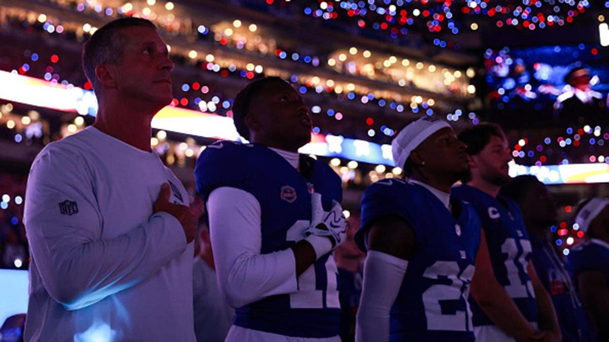 John Harbaugh and Giants players stand on the sideline during the national anthem at MetLife Stadium.