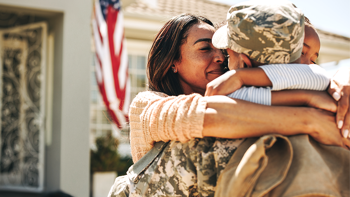 Military service member embraces family in stock image.