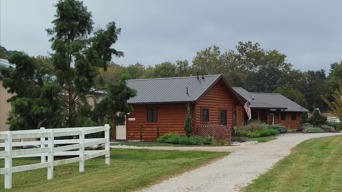 Wooden rental cabin surrounded by white fencing and greenery at a Missouri horse ranch.