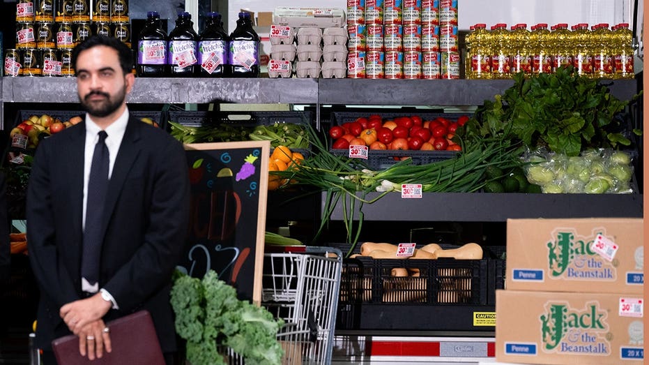Zohran Mamdani, mayor of New York, stands behind groceries at a community food distribution center.