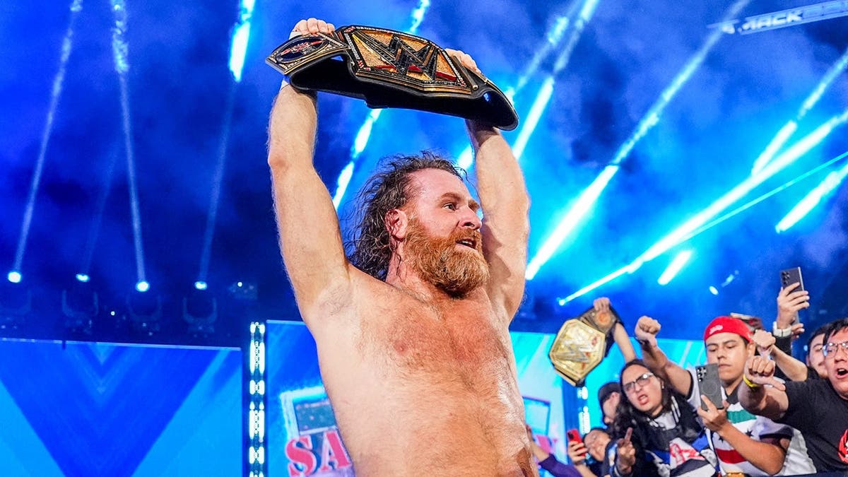Sami Zayn celebrates with the WWE Championship belt in an arena.