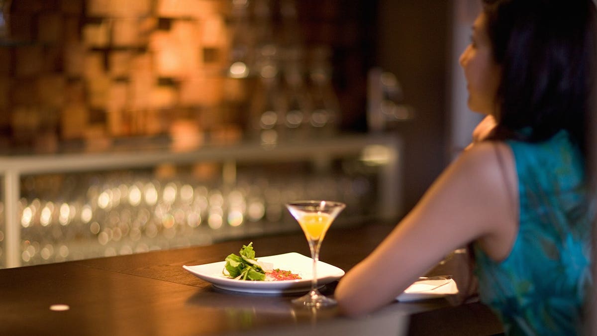 Woman eats alone at bar with cocktail.