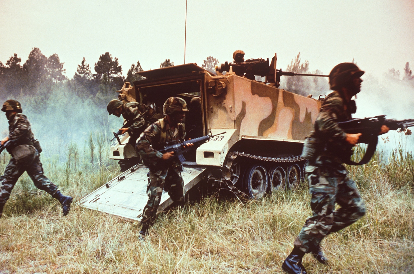 US Army soldiers charge out of the back of an M113 APC during training in 1984
