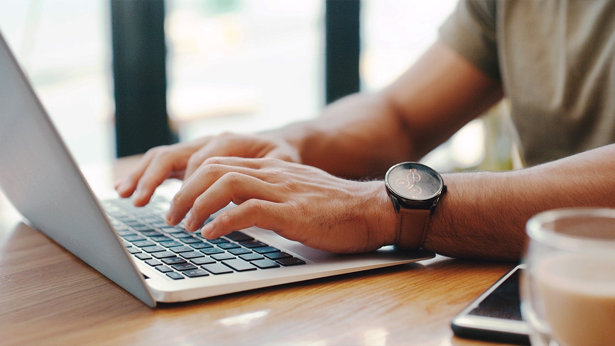 A person wearing a watch types on a laptop.