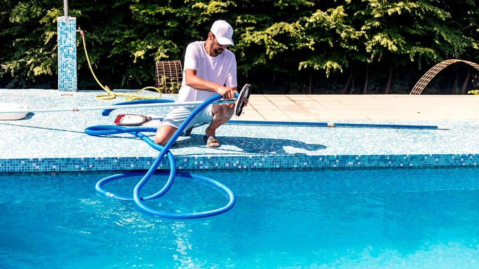 A man kneels on the side of a pool with equipment.